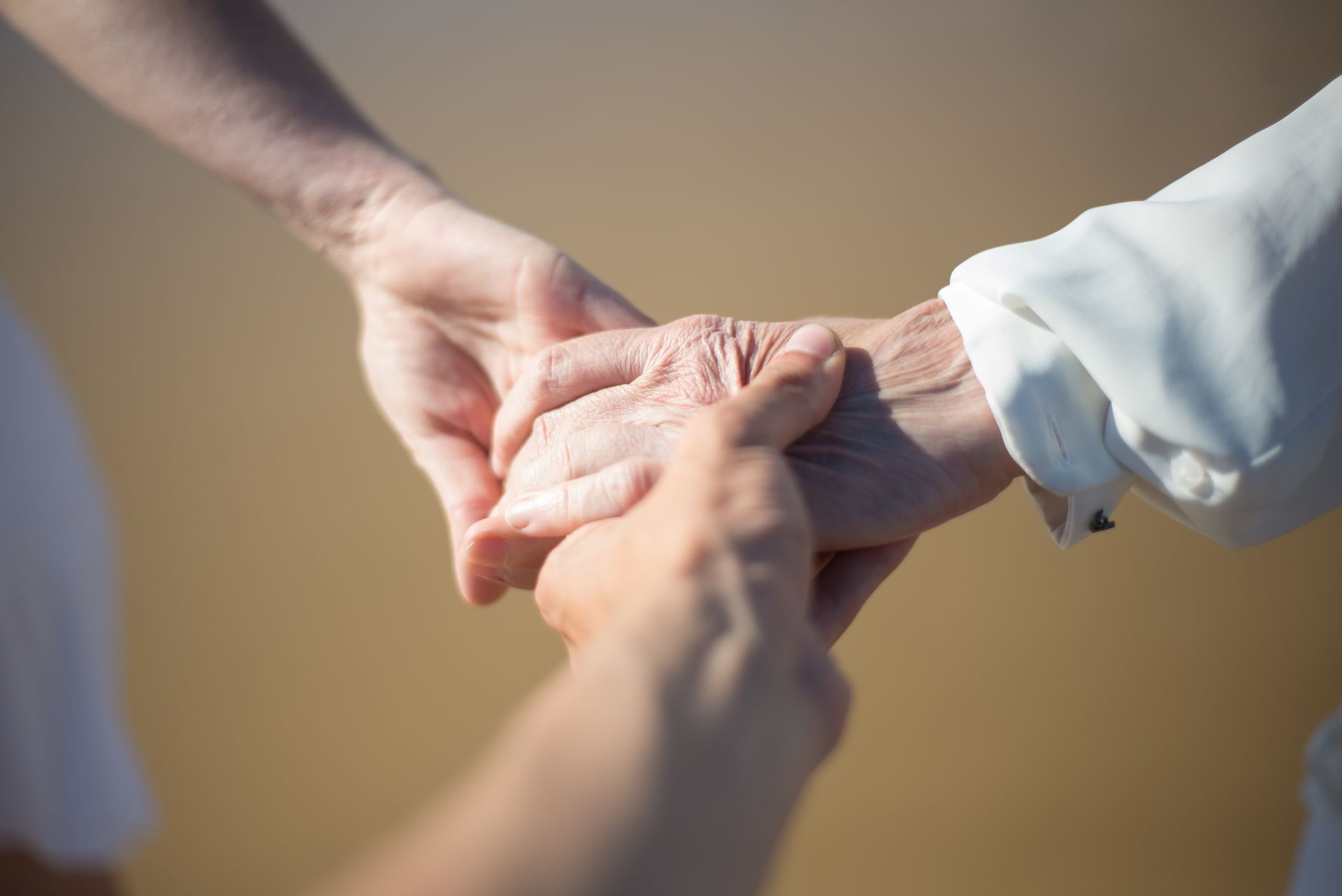 A pair of younger hands gently holding an older person's hand